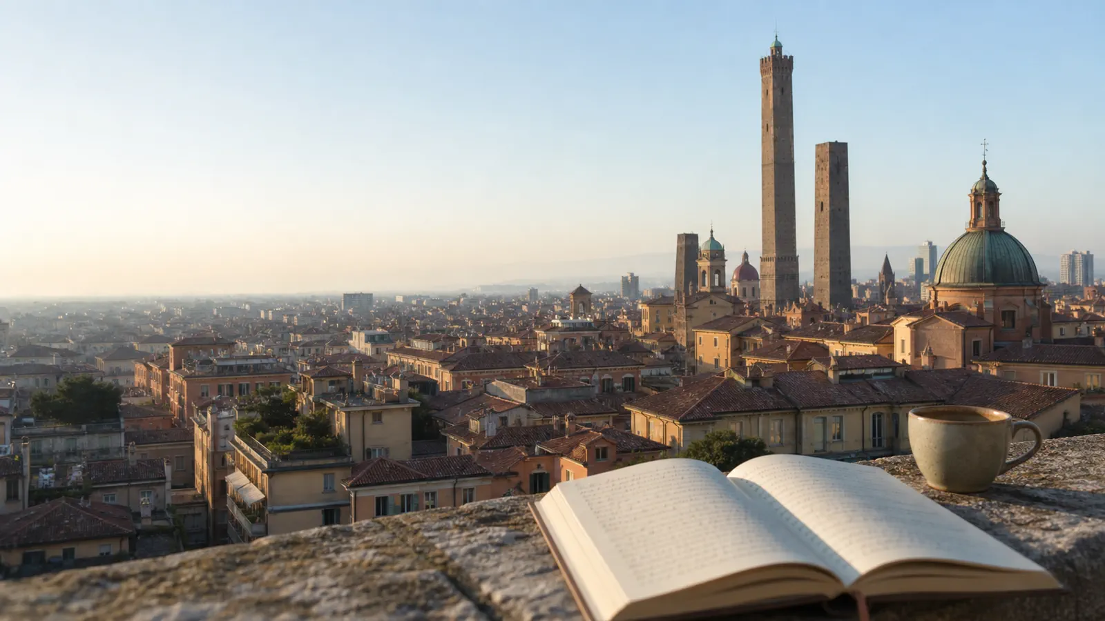 An open book and a cup resting on a stone ledge, with Bologna towers and domes in the distance