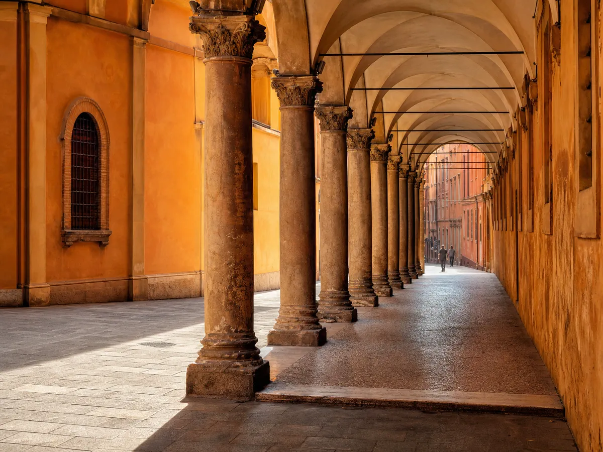 A long stone portico with arched ceilings and people walking beneath it