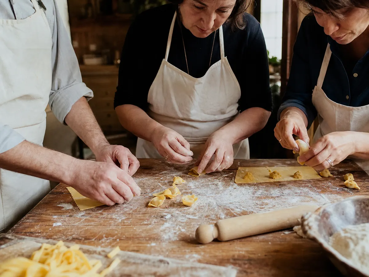 Three people in aprons making pasta on a floured wooden table